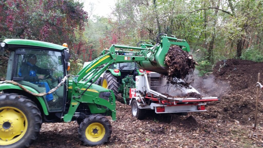 Tracteur John Deere 4720 chargeant du compost fumant dans un broyeur. Travaux forestiers avec chargeur frontal 400CX.