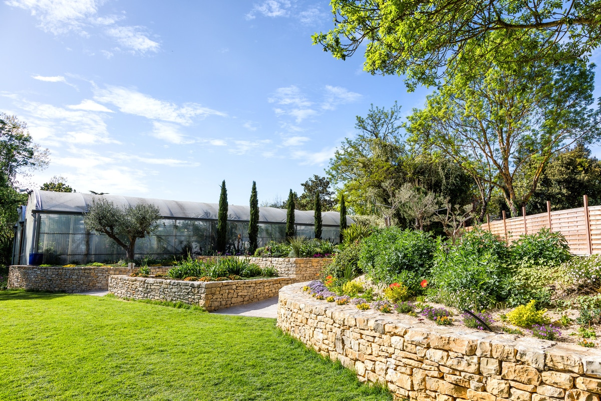 Terrasse en bois: créez votre jardin balcon luxuriant. Balcon ensoleillé avec plancher en bois, parterre de fleurs roses et jaunes luxuriantes. Fauteuil moderne gris, vue sur la ville.