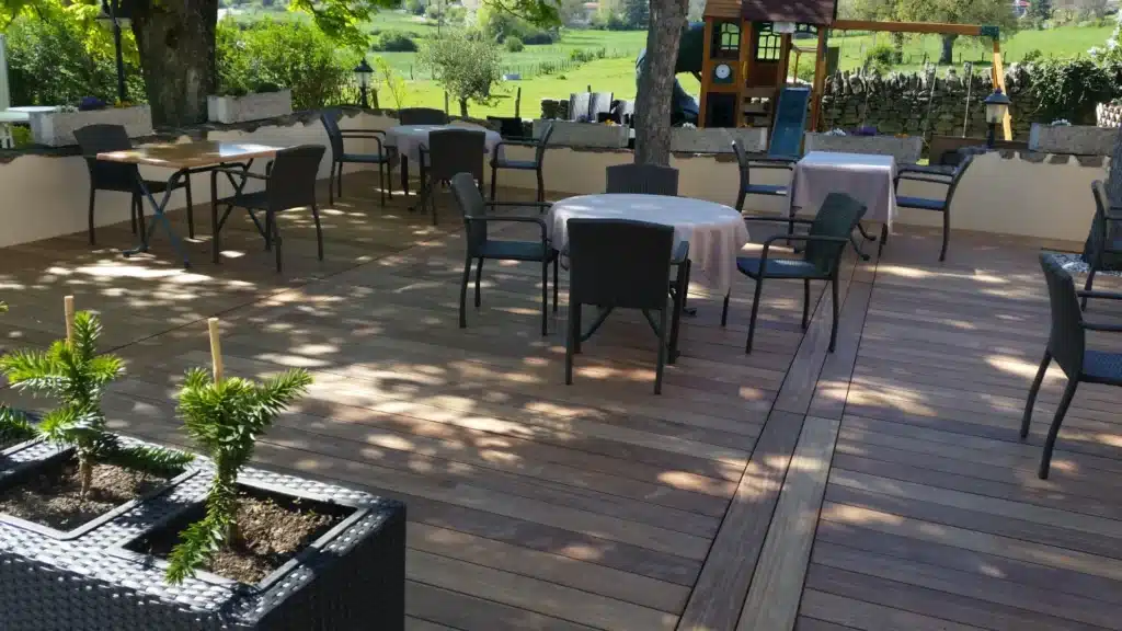Terrasse de restaurant en bois avec tables dressées et vue sur une aire de jeux et la campagne environnante.